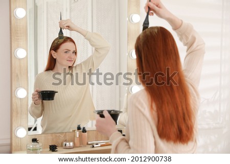 Young woman dyeing her hair with henna near mirror