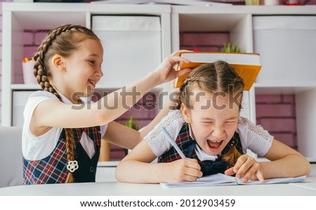 Two girls are sitting at one desk in the classroom. One girl hits another on the head. The problem of bullying at school and the aggression of children concept. Royalty-Free Stock Photo #2012903459