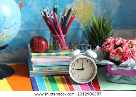 Back to school time, school table with accsesories, pencils and apple snack, roses and alarm clock on the world map background 