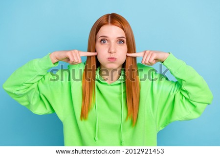 Photo of impressed childish young woman wear green sweatshirt fingers pressing bloated cheeks isolated blue color background