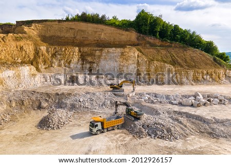 Open pit mining of construction sand stone materials with excavators and dump trucks.