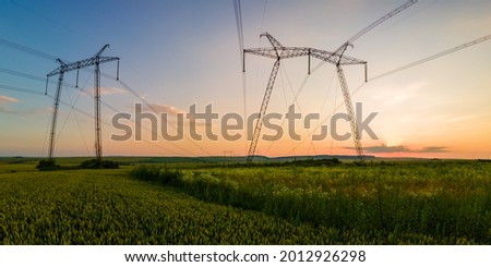 Dark silhouette of high voltage towers with electric power lines at sunrise.