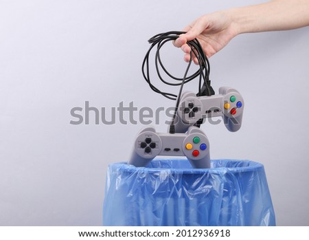 Hand throws plastic gamepads into trash bin with package on gray background