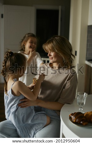 Young beautiful mother with two pretty daughters on the kitchen. Happy family breakfast. Stylish interior. Good relationships. Funny children. Love and care.  Europeans.  Live and natural picture