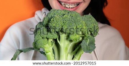 Woman's mouth with broccoli between big white teeth