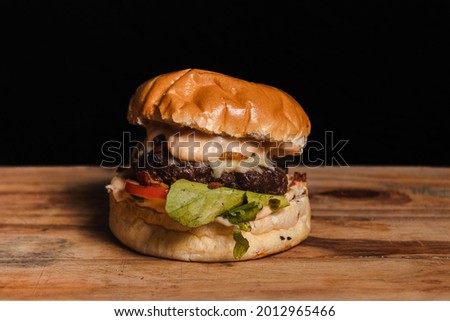 Small hamburger with lettuce and tomato on a wooden table with black background.