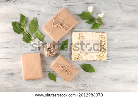 Holiday composition. Ceramic vintage photo frame, gifts wrapped in craft paper, bandaged with jute rope, white flowers on a wooden background, flat lay, copy space.