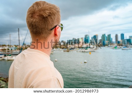A young man on the pier overlooking downtown San Diego on a cloudy day.