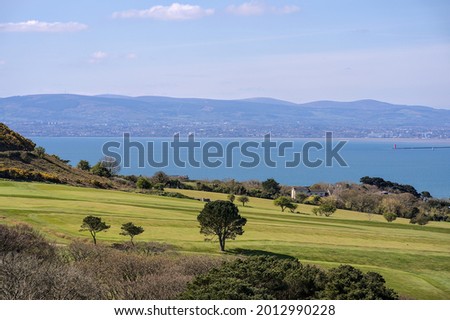 Beautiful scenic aerial-like bright view of golf course with trees, Irish sea, Dublin bay, Poolbeg lighthouse and Dublin Mountains seen from Howth, Dublin, Ireland. Irish landscapes