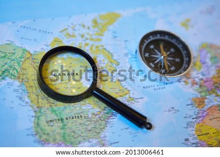 The magnifying glass is located on the world map and magnifies the country of Canada. There's a compass next to it. Concept of travel and news about the selected country. Royalty-Free Stock Photo #2013006461