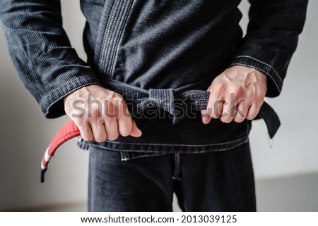 Front view of hands of unknown caucasian man in kimono gi standing while holding and tie knot black bjj belt brazilian jiu jitsu concept copy space Royalty-Free Stock Photo #2013039125