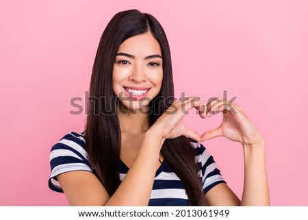 Photo of excited charming young lady dressed striped clothes smiling showing fingers heart isolated pink color background