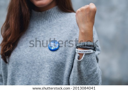 Closeup image of a young woman showing Covid-19 vaccinated wristband and  brooch