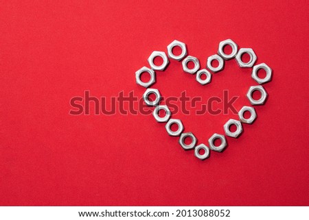 Heart made of steel nuts on red background, concept of love, peace and kindness, leaving space for advertising text
