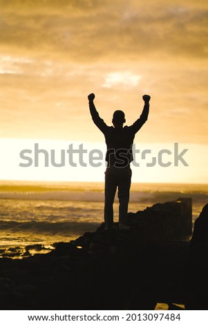happy successful MAN  in YES POSE on beach rocks AT THE ocean WITH arms wide open enjoying life
