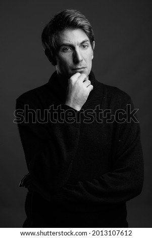 Studio shot of handsome man wearing coat for cold weather against gray background in black and white