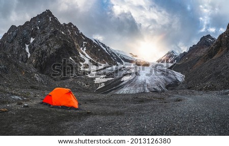 Panoramic view of an orange fortified tent on the background of a glacier on a high-altitude plateau. Extreme overnight stay in the mountains.