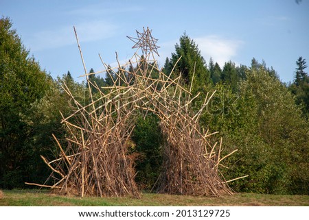 An arch made of branches with a star at the top against the background of the forest. A neo-pagan harvest ritual at sunset. Royalty-Free Stock Photo #2013129725