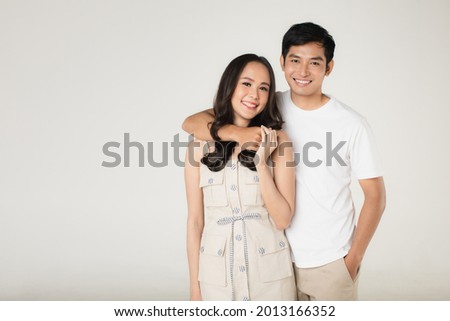 Portrait of young attractive Asian couple, man wearing white t shirt and beige pants, woman wearing beige dress. Man arm around woman on white background. Concept for pre wedding photography.