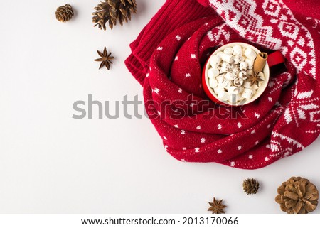 Top view photo of red cup of hot drinking with marshmallow and cinnamon stick wrapped in red sweater with ornament pine cones and anise on isolated white background with copyspace