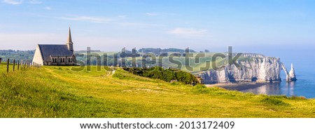 Panoramic view of the cliffs in Etretat, Normandy, with Notre-Dame de la Garde chapel overlooking the bay and the Aval cliff, its arch and the Needle in the distance. Royalty-Free Stock Photo #2013172409