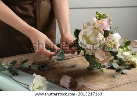 Florist creating beautiful bouquet at wooden table indoors, closeup Royalty-Free Stock Photo #2013217163
