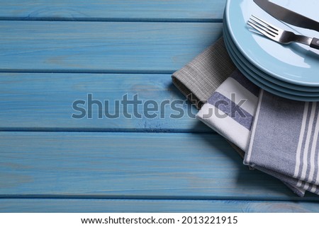Different kitchen towels and stack of plates with cutlery on blue wooden table. Space for text