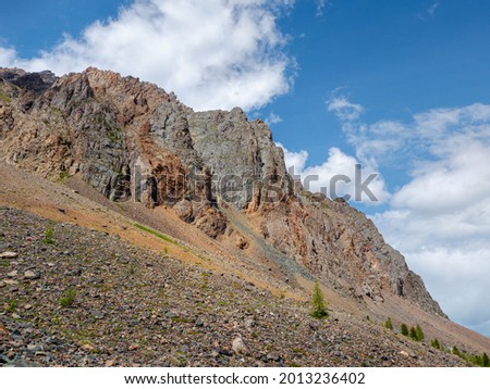 Atmospheric landscape with rocky mountain wall with pointy top in sunny light. Loose stone mountain slope in the foreground. Sharp stony mountains. Royalty-Free Stock Photo #2013236402