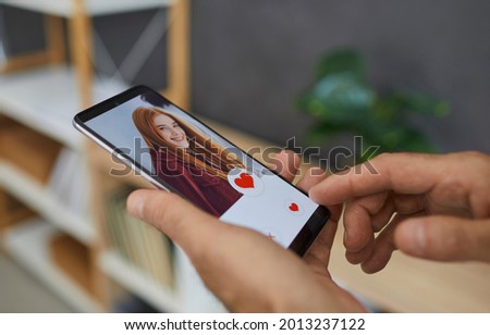 Love online concept. Closeup man pressing red heart button and giving a like to pretty ginger redhead young girl's picture on dating website or mobile phone app. Hands holding cellphone in close up