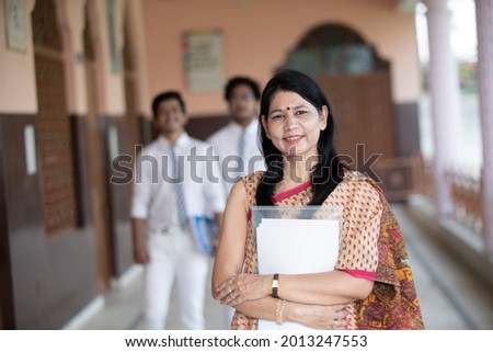 Confident smiling Indian school teacher with students in background