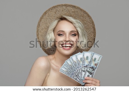 A girl with a short haircut in a hat holds a bundle of dollars in her hands