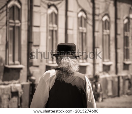 Old vintage sepia picture of a man with long gray hair and a black hat on his head. Back view of a senior man.
