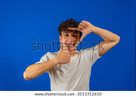 Photo of charming cute young guy dressed white shirt showing camera shot gesture smiling isolated blue color background. Gesture concept