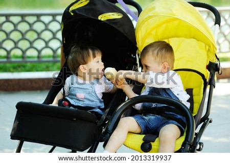 Toddler boy sharing ice cream with his baby sister during ride in double stroller in the summer city park