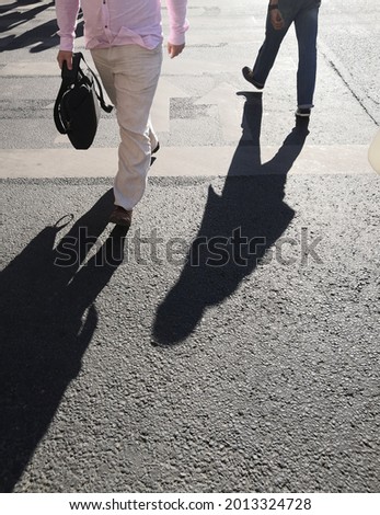 Legs and shadows of citizens crossing asphalt road at zebra crosswalk 