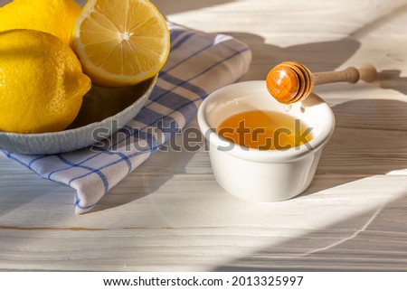 Honey in white bowl with honey dipper or stick, lemon and mint in blue and white linen towel as background. Organic natural ingredients concept.