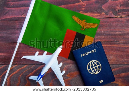 Flag of Zambia with passport and toy airplane on wooden background. Flight travel concept