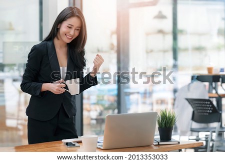 Beautiful asian woman celebrate with laptop while standing in office, successful business concept.