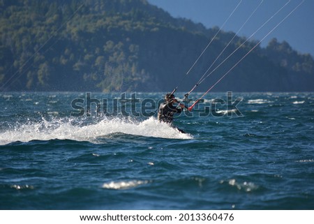 man kitesurfing in Moreno lake near Bariloche, in the Zul water leaving water trail with wetsuit