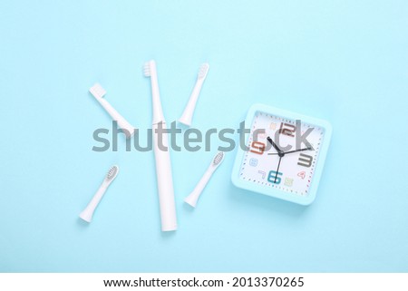 Ultrasonic plastic toothbrush with replaceable heads and alarm clock on blue background. Dental care concept. Top view