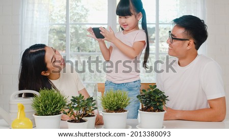 Happy cheerful Asian family dad, mom and daughter using smart phone taking pictures of plant in garden at house. Self-isolation, stay at home, social distancing, quarantine for coronavirus prevention.