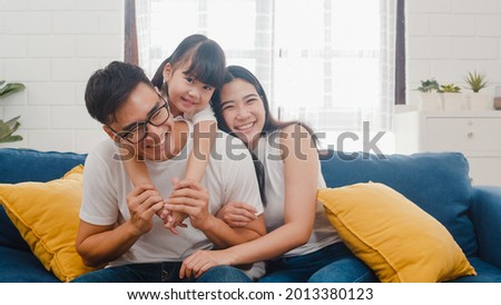 Happy cheerful Asian family dad, mom and daughter having fun cuddling and video call on laptop on sofa at house. Self-isolation, stay at home, social distancing, quarantine for coronavirus prevention. Royalty-Free Stock Photo #2013380123