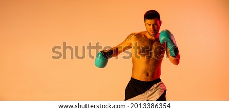 Sparring match. One man, professional boxer in sports shorts and gloves boxing isolated on yellow studio background neon light. Concept of sport, activity, movement, wellbeing. Copyspace, ad