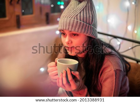 Indoor image of an Asian, Indian beautiful, serene young woman looking away and contemplating while drinking and holding a cup of coffee in winter season at home. She is wearing warm clothes. Royalty-Free Stock Photo #2013388931