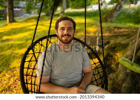 Photo of a attractive young guy relaxing on a hammock in the middle of nature. It is a summer day in the forest and he has a happy smile