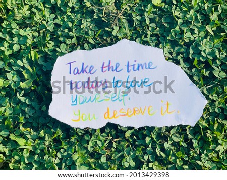 Take the time today to love yourself! You deserve it! Handwritten message. Green grass as background.