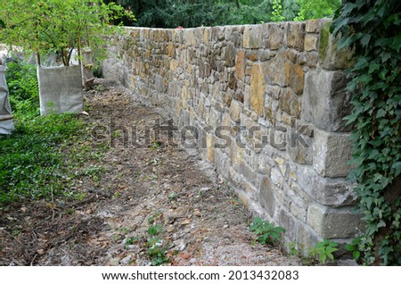 an old stone wall is being reconstructed between the two plots. the stones are dismantled and re-glued to the cement mortar. stonemason builds a wall in the park. the joints are repaired and the bush Royalty-Free Stock Photo #2013432083