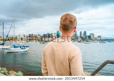 A young man on the pier overlooking downtown San Diego on a cloudy day.