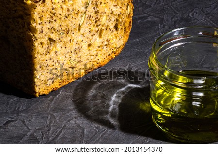 slice of rustic natural yeast-free bread with flax, poppy seeds, sesame seeds, millet, pumpkin and sunflower seeds, with olive oil in a glass jar, on a black background, hard light, photo in a low key