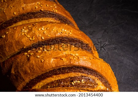 Unusual two-color fresh loaf of bread on a black background, photo in a low key in hard light, close-up